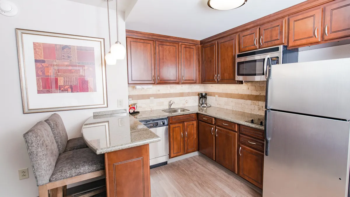 An open-concept kitchen and dining area with rich wooden cabinets, sleek granite countertops, and a bar seating area that connects seamlessly to the living space. Modern appliances and cozy breakfast nooks hint at shared cooking experiences and casual dining, reinforcing a sense of togetherness.