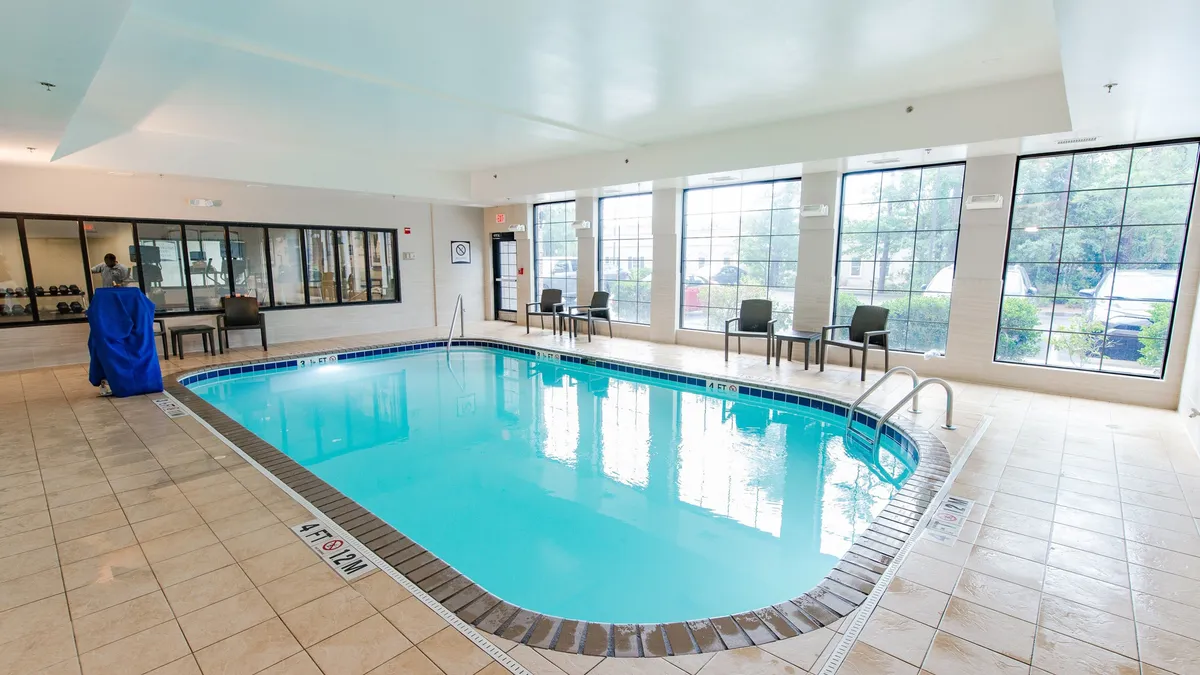 A bright, spacious indoor swimming pool area featuring large windows that let in natural light, a comfortable seating area along the poolside, and an inviting swimming pool. The space is ideal for both relaxing swims and social gatherings, reflecting a sense of calm and refreshment.